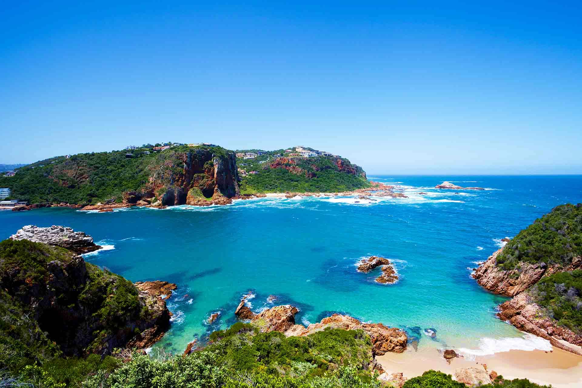 South Africa Visa Scenic coastal landscape of a rocky headland with turquoise waters, sandy beach, and lush green vegetation in South Africa